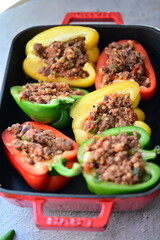 Close-up of Mediterranean-style stuffed bell peppers arranged in a red baking dish, ready for the oven. This homemade meal scene on a light background captures the essence of fresh, flavorful cooking