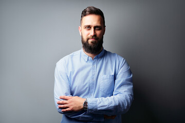 Confident Bearded Man in Casual Outfit Standing Against Gray Wall Background