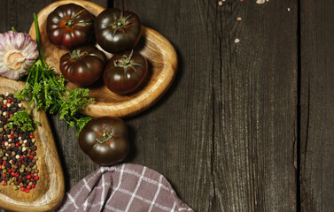 Black tomatoes and different spices on wooden table