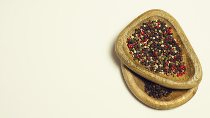 Four-color and black pepper on wooden plates, light background.