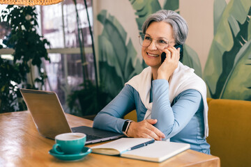 Confident mature woman smiling during phone conversation in modern workspace