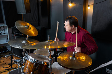A man actively playing a drum kit in a professionally lit music studio, captured mid-performance. The scene portrays focus, musicality, and passion for percussion music in a creative environment