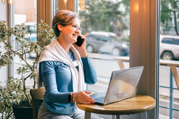 Senior woman with laptop opening cafe door, friendly smile and casual business fashion