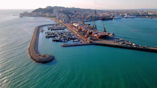 Aerial view of the fishing port of Durr&euml;s, Albania, as seen from the sea. The harbor is protected by a curved breakwater and filled with docked fishing vessels.