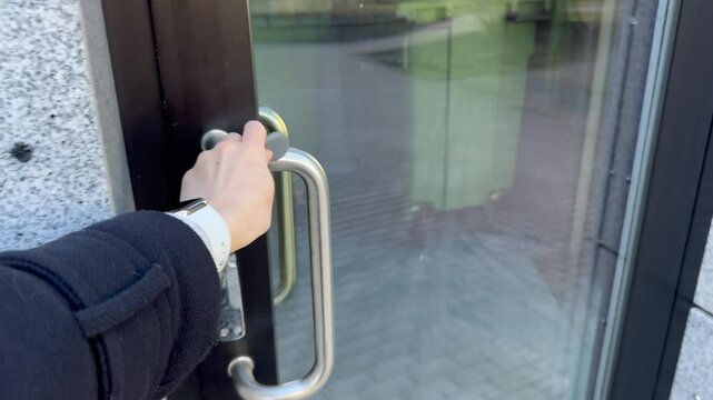 Close-up of female hand using grey key fob on smart door entry device. Red light changes to green. Glass door, granite wall background. Building security in action. Modern access control concept
