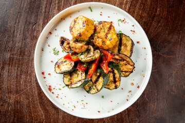Grilled vegetables on a white plate, including corn, zucchini, bell peppers, and mushrooms, garnished with herbs and spices. The dish is colorful and appetizing, showcasing healthy and delicious food