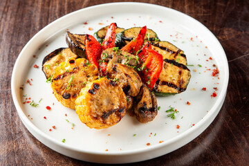Grilled vegetables on a white plate, including corn, zucchini, bell peppers, and mushrooms, garnished with herbs and spices. The dish is colorful and appetizing, showcasing healthy and delicious food
