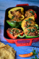 Close-up of vibrant stuffed bell peppers filled with seasoned ground beef, bulgur, and melted cheese. The dish is baked and served in a red baking dish placed on a blue rustic  food background. yummy