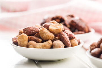 Nuts coated in sugar and honey in bowl on white table.