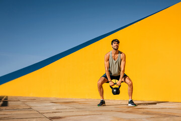 Hispanic athlete performs kettlebell workout against colorful background in outdoor setting