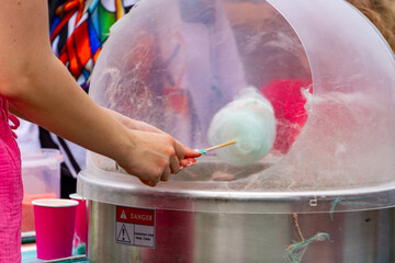 person preparing cotton candy using a spinning machine at a fair. The background shows colorful...