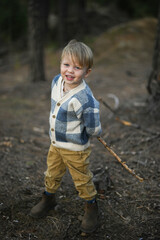 Little boy in a sweater plays with a stick in the forest. Pure childhood joy, imagination, and connection to nature. Autumn colors and outdoor freedom.