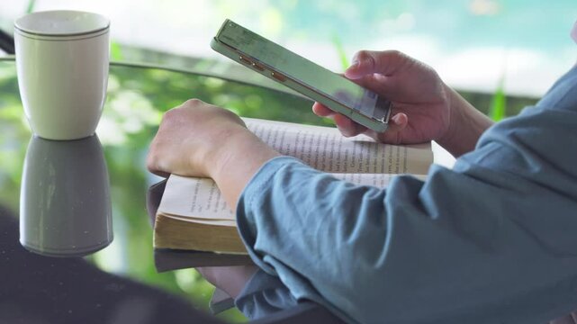 A person is reading a book and looking at their phone with relaxed and leisurely scene