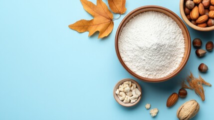 Fototapeta premium Artisan food setup: flour with decorative leaves and nuts over soft blue base