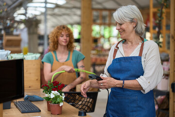 Senior cashier scanning products at checkout in a sunny plant nursery