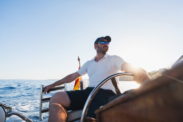 Man steering recreational boat at sea during golden hour, wearing sunglasses and cap