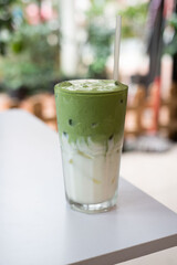 A refreshing glass of green tea with milk and a straw resting on a table