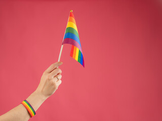 Woman with wedding ring holding rainbow flag on pink background. 