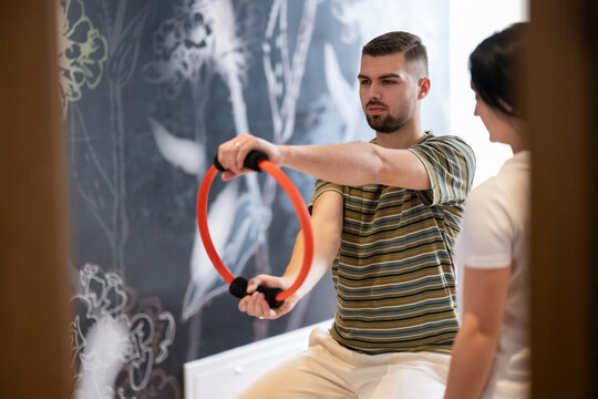Physical Therapy Session with Resistance Ring.A male patient performing arm exercises using a resistance ring under supervision during a rehabilitation session.