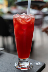 A glass filled with red liquid, ice, and a straw, placed on a table