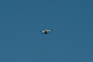 A small drone flying high in the clear blue sky, captured in sharp detail against a minimalistic background. A peaceful, modern scene of technology in open air.