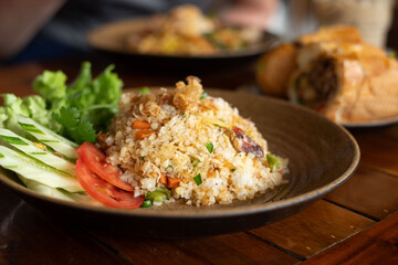 A plate of fried rice with fresh vegetables sits on a wooden table