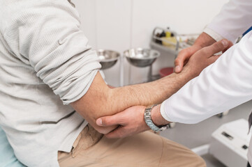 traumatologist examines male patient's elbow in hospital. range of motion test, pain, arm injury....