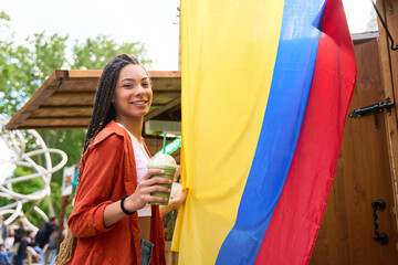 Young latin woman holding a smoothie near colombian flag at summer festival