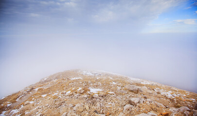 Misty mountain peak with snow patches emerging through dramatic clouds
