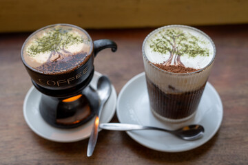 Two cups of coffee on saucers with spoons are on a table