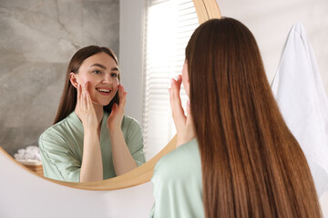 Beautiful woman looking at herself in mirror indoors