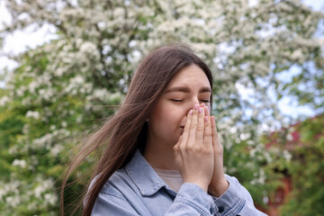 Woman suffering from seasonal pollen allergy near blossoming tree on spring day