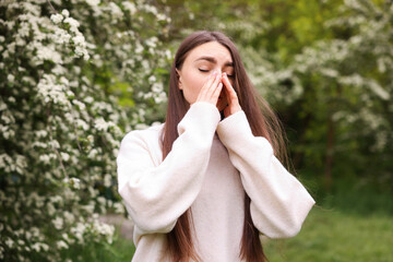 Woman suffering from seasonal pollen allergy near blossoming shrub on spring day