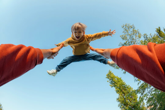 POV view, father tosses high and catches his excited joyful son. Energetic young boy with arms outstretched flying midair against a blue sky, thrown by parent during playful outdoor moment. 