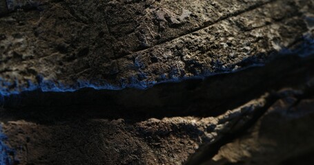 Close-up of layered rock with deep cracks and blue-toned lighting effects