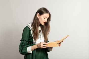 A young woman in a vintage green dress inspects a wooden box with curiosity. The indoor setting...