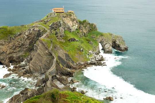 Scenic view of San Juan de Gaztelugatxe, a dramatic islet on the Basque coast of Spain. The image captures the winding stone staircase leading to the historic hermitage atop the rocky island, surround