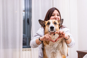 Smiling woman making heart shape with hands and her dog at home