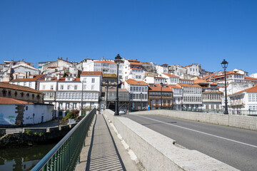 Traditional Galician white buildings seen from Ponte Vella bridge over Mandeo River in Betanzos, Spain, surrounded by lush greenery.