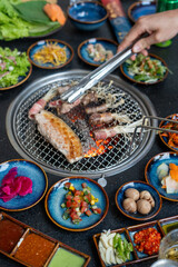 A person is currently cooking meat on a grill using tongs