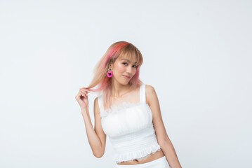 Trendy Southeast Asian woman in pastel fashion twirling her dyed hair and smiling with a coy, playful expression. Isolated on a light background.