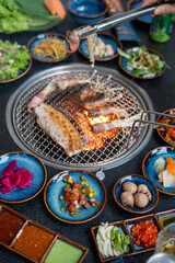 A person is grilling meat with plates of food around them