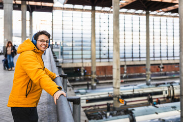 Young traveler wearing headphones enjoying train station view