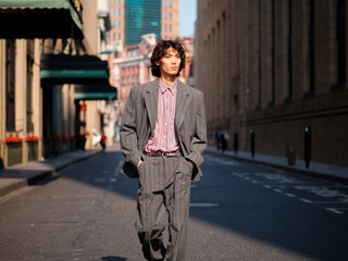 Portrait of handsome Chinese young man wearing gray suit walking in the street, young guy with black curly hair with urban background. Male fashion, cool Asian young man lifestyle.