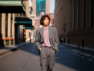 Portrait of handsome Chinese young man wearing gray suit walking in the street, young guy with black curly hair with urban background. Male fashion, cool Asian young man lifestyle.