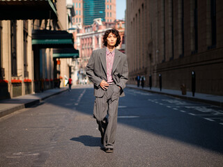 Portrait of handsome Chinese young man wearing gray suit walking in the street, young guy with black curly hair with urban background. Male fashion, cool Asian young man lifestyle.