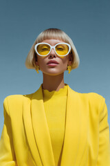 Fashion model wearing yellow suit and sunglasses posing under blue sky