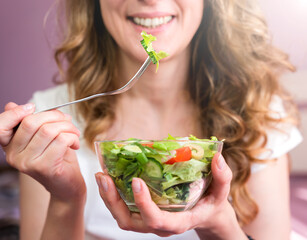 Smiling young woman eating salad for breakfast. Healthy eating concept. Close-up. Selective focus.