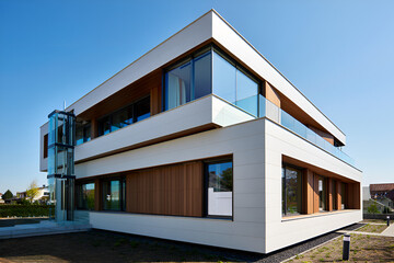 Fototapeta premium Modern building with glass elevator and wooden accents under blue sky