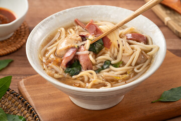 Taiwanese squid thick noodle soup in ceramic bowl on wooden table background.